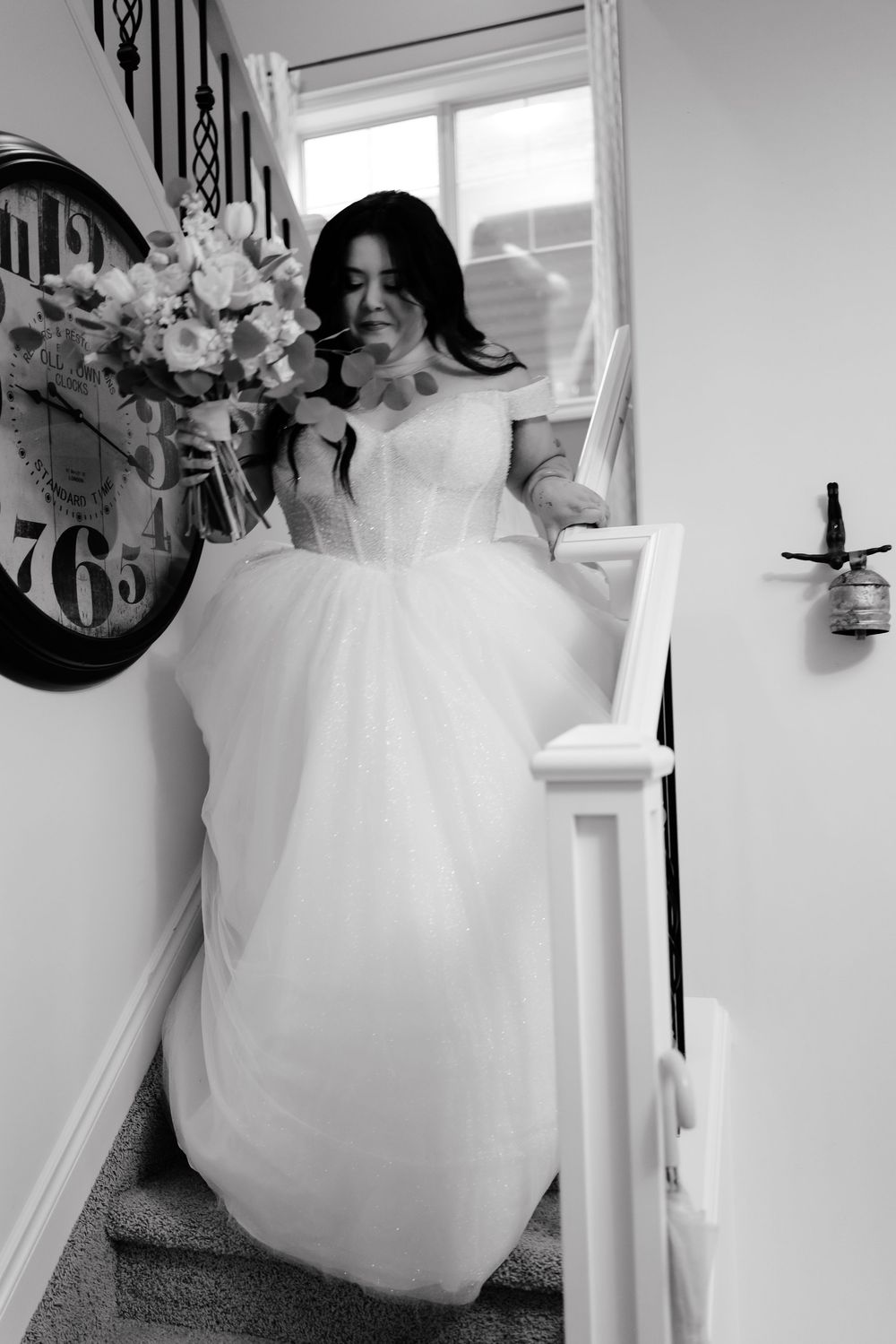 Black and white photo of a bride in a white ball gown descending stairs holding a bouquet.