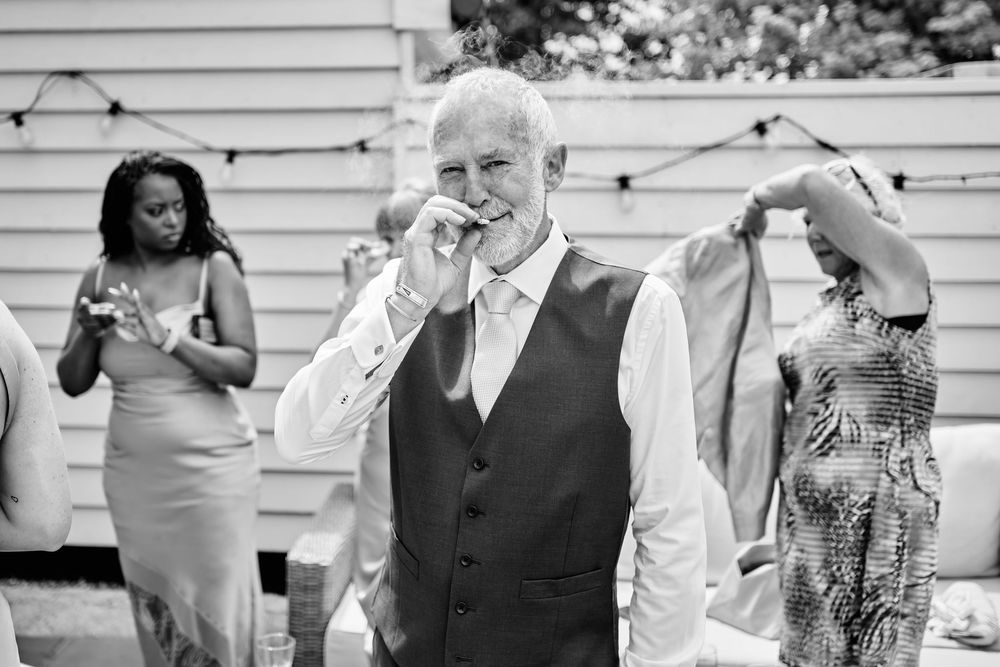 Man in vest sipping a drink at an outdoor wedding reception in black and white photo.