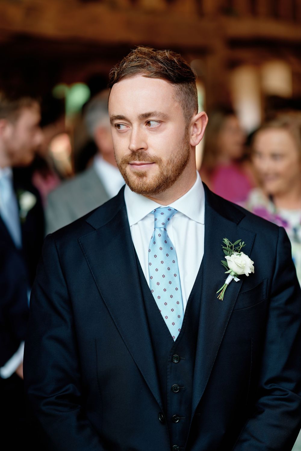 Groom in navy suit with blue tie and white boutonniere at wedding ceremony.