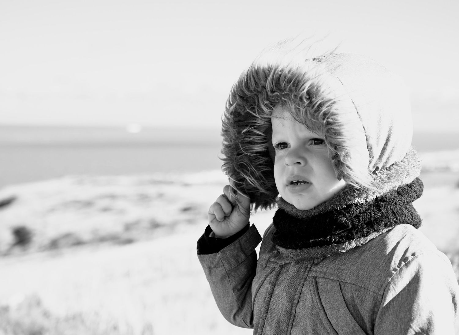 Enfant en manteau à capuche fourrée, fond plage
