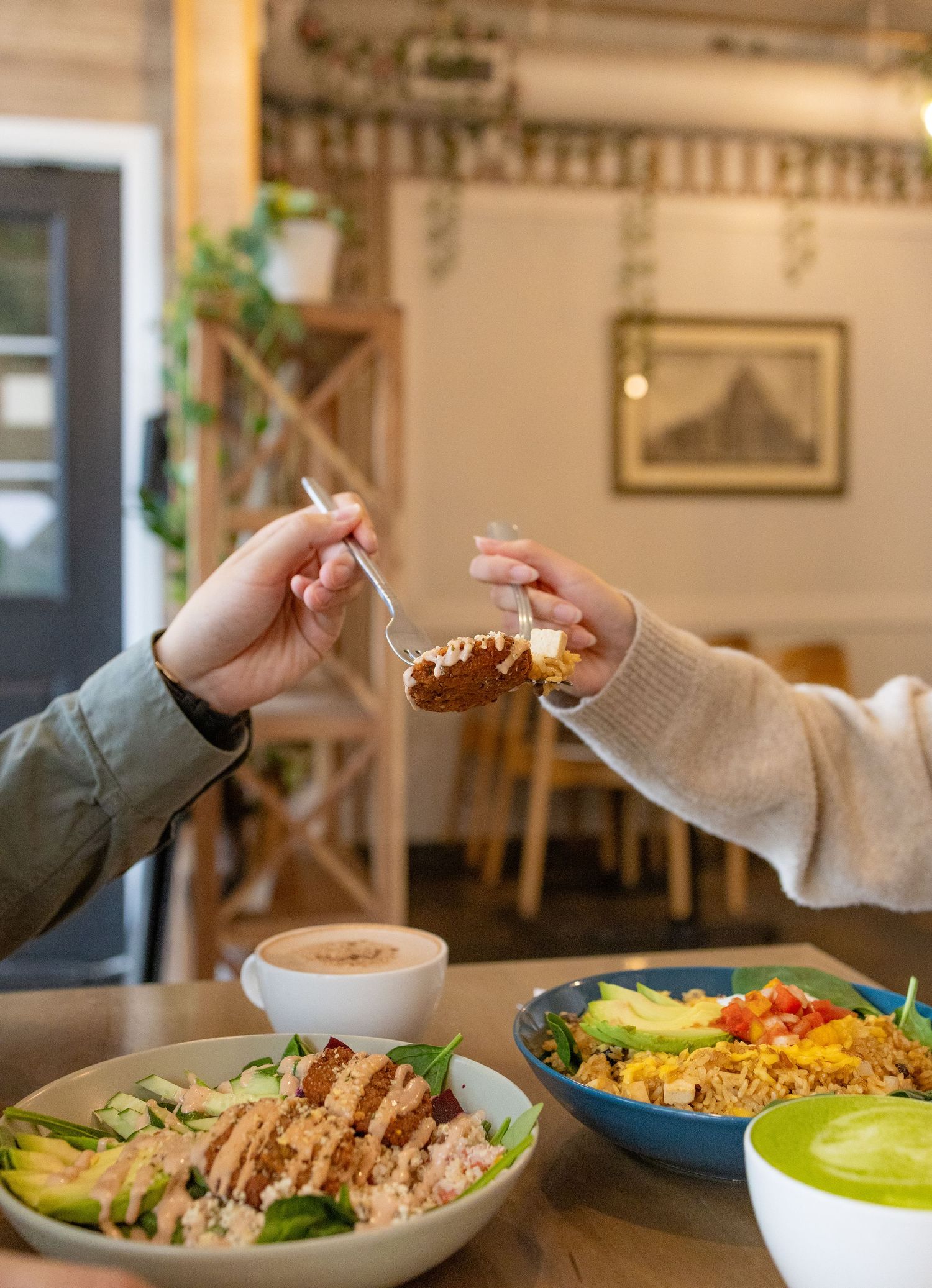 Two people sharing a meal at a cafe table with colorful grain bowls, avocado, and grilled chicken.