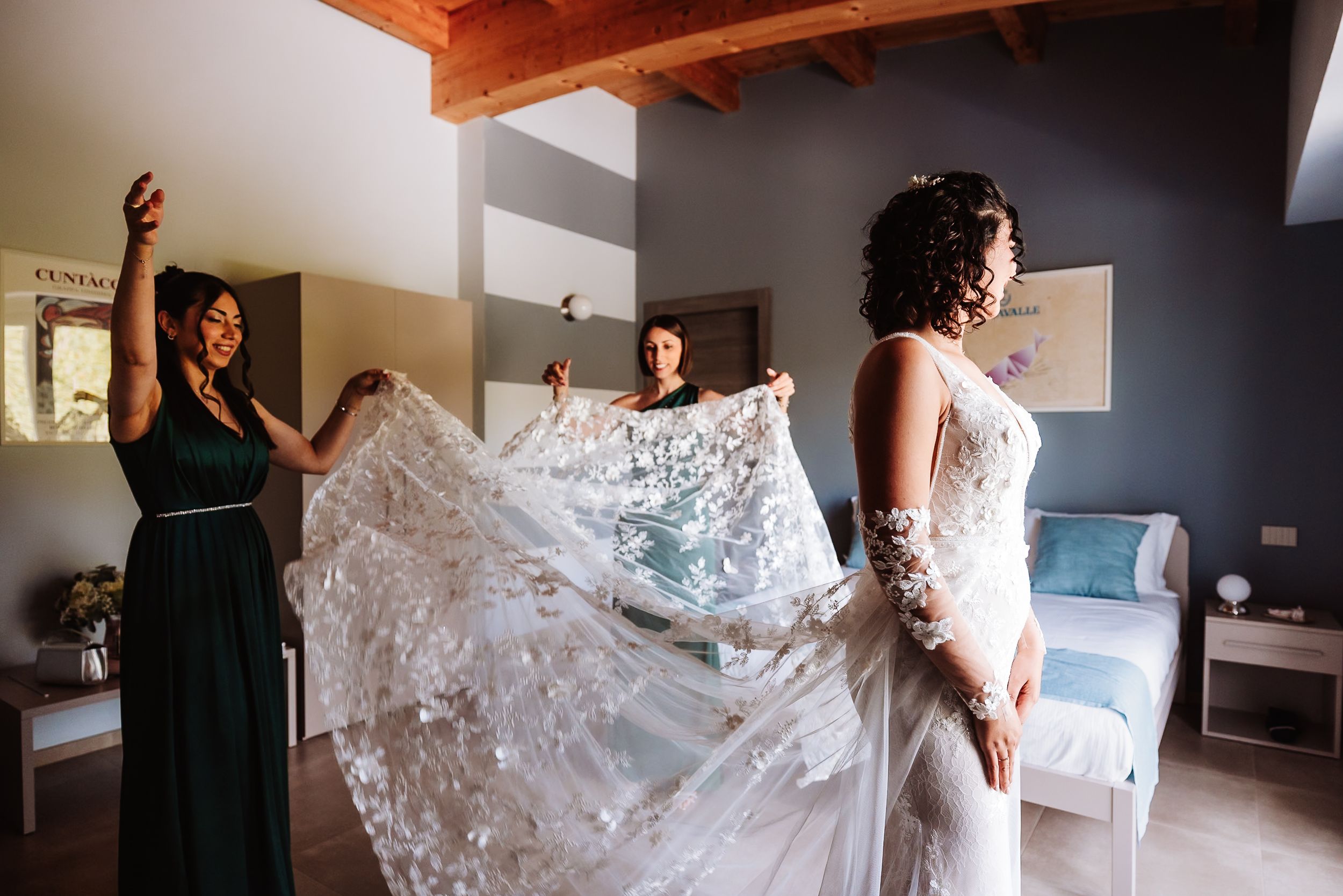 Bridesmaids helping bride with lace wedding veil in elegant bridal suite before ceremony.