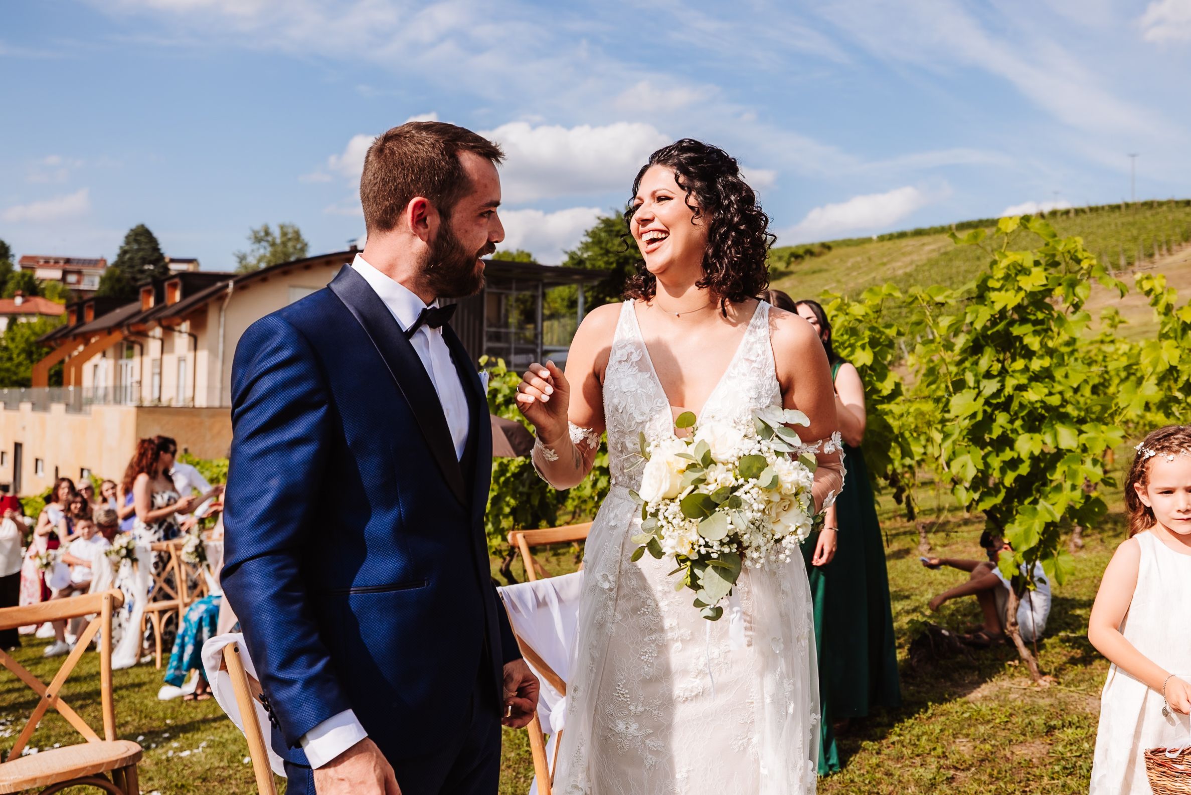 Bride and groom share a joyful moment at an outdoor vineyard wedding ceremony, bride holding a white bouquet.