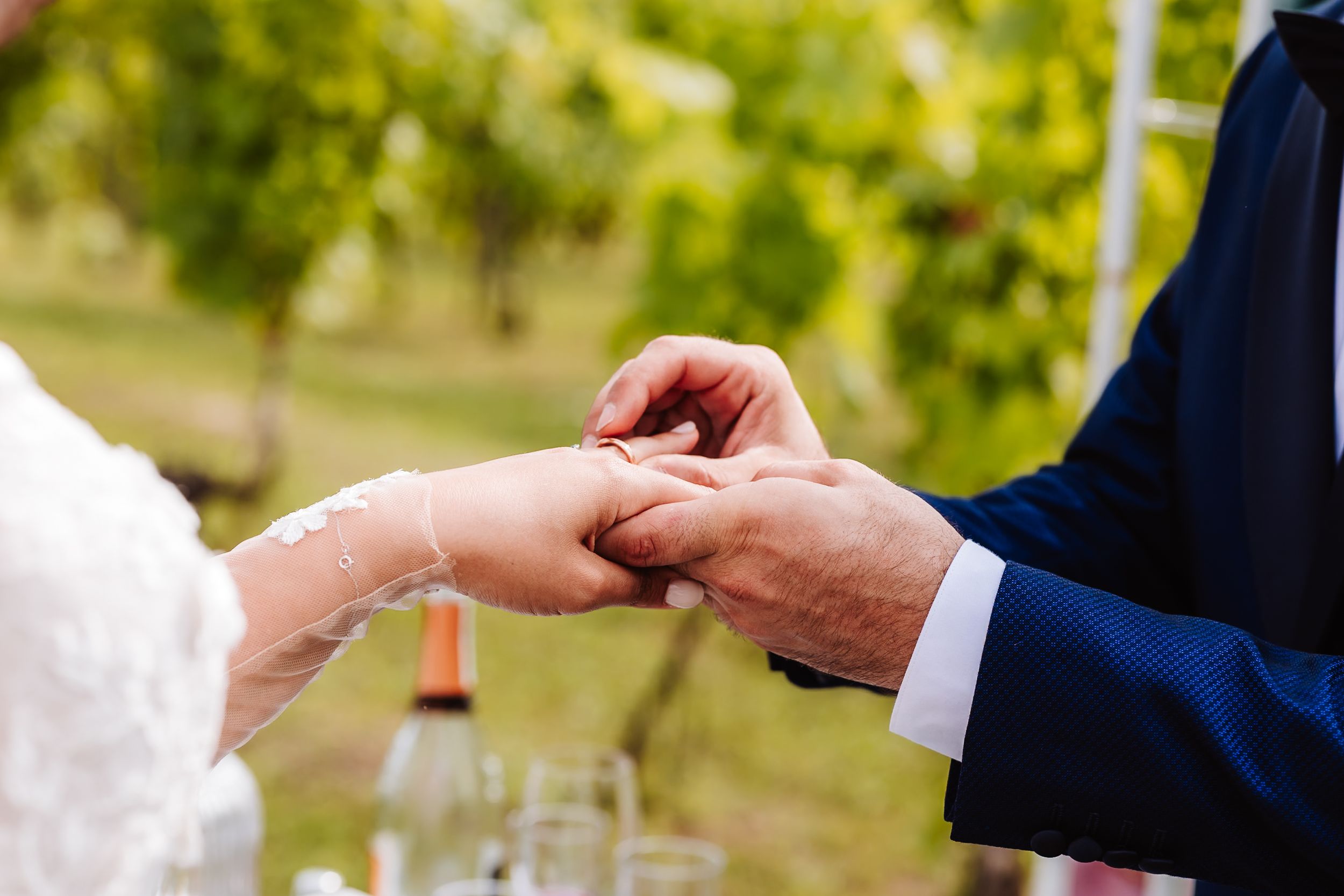Groom placing a wedding ring on bride's finger during an outdoor vineyard ceremony.