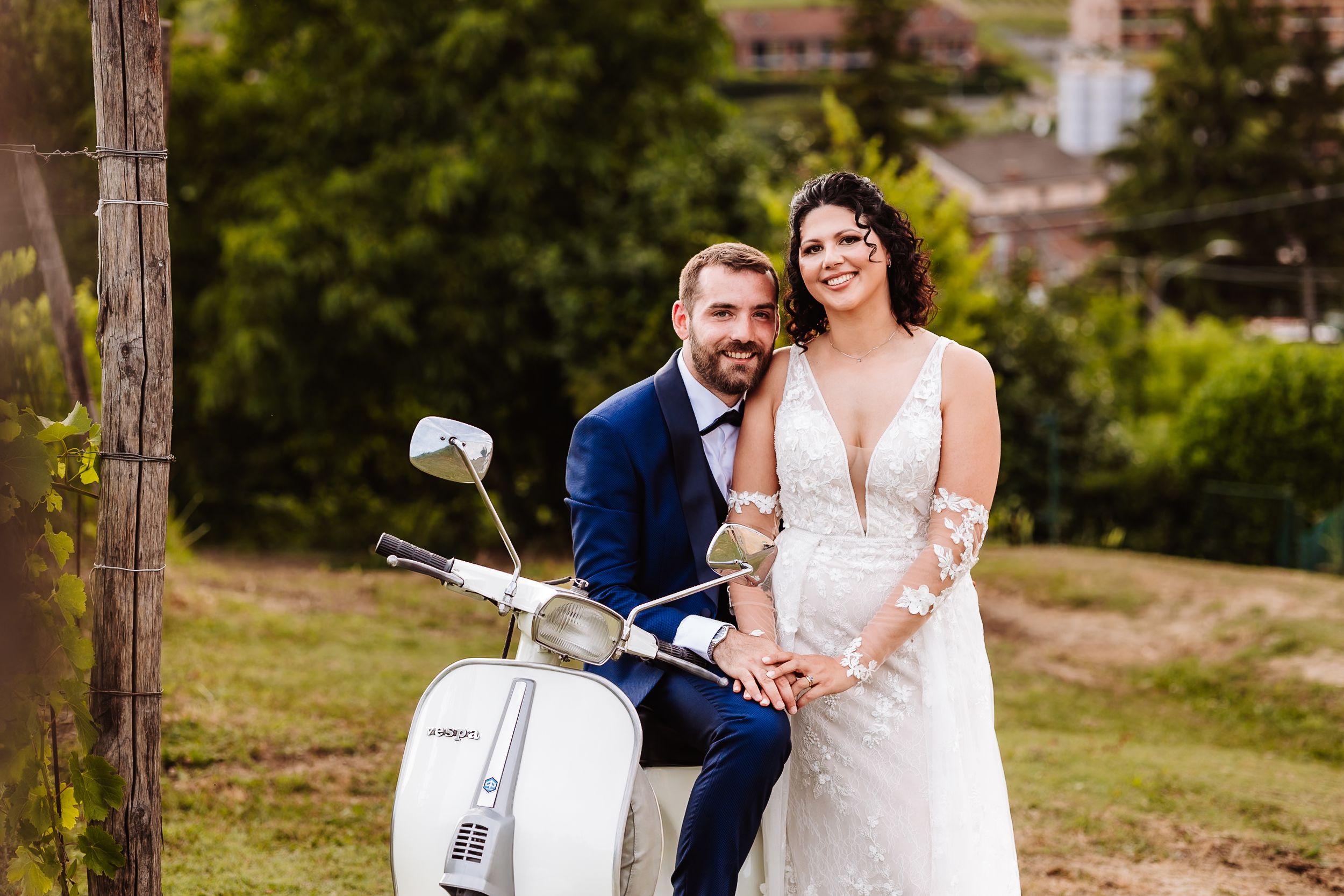 Bride and groom posing together on a white Vespa scooter outdoors on their wedding day.