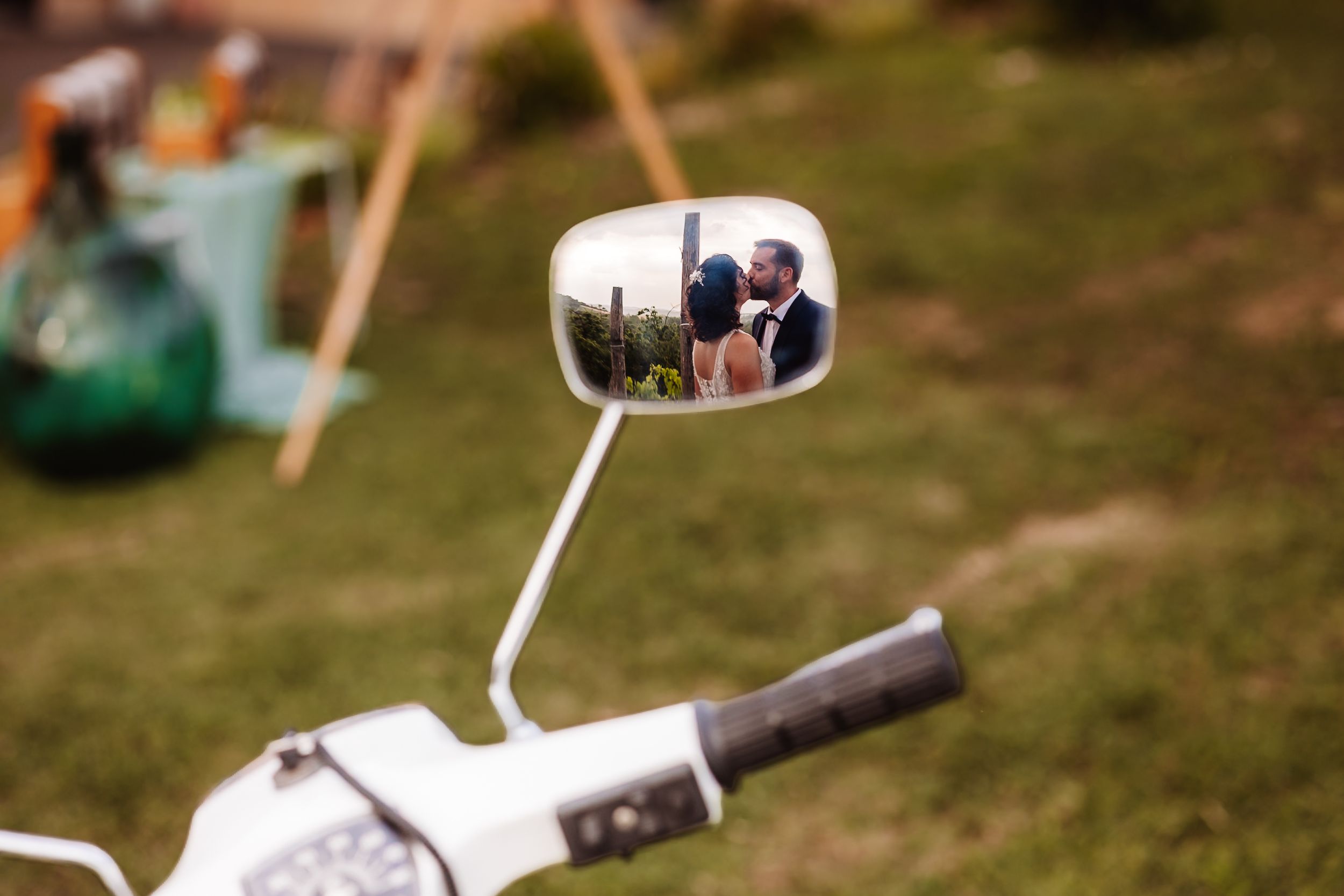 Wedding couple reflected in a vintage scooter mirror on a lush green lawn.