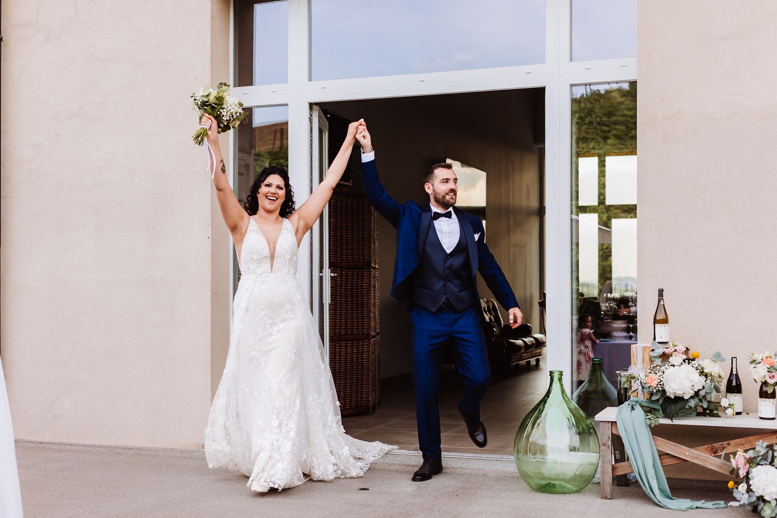 Bride and groom celebrating their grand entrance at an outdoor wedding reception, raising hands joyfully.