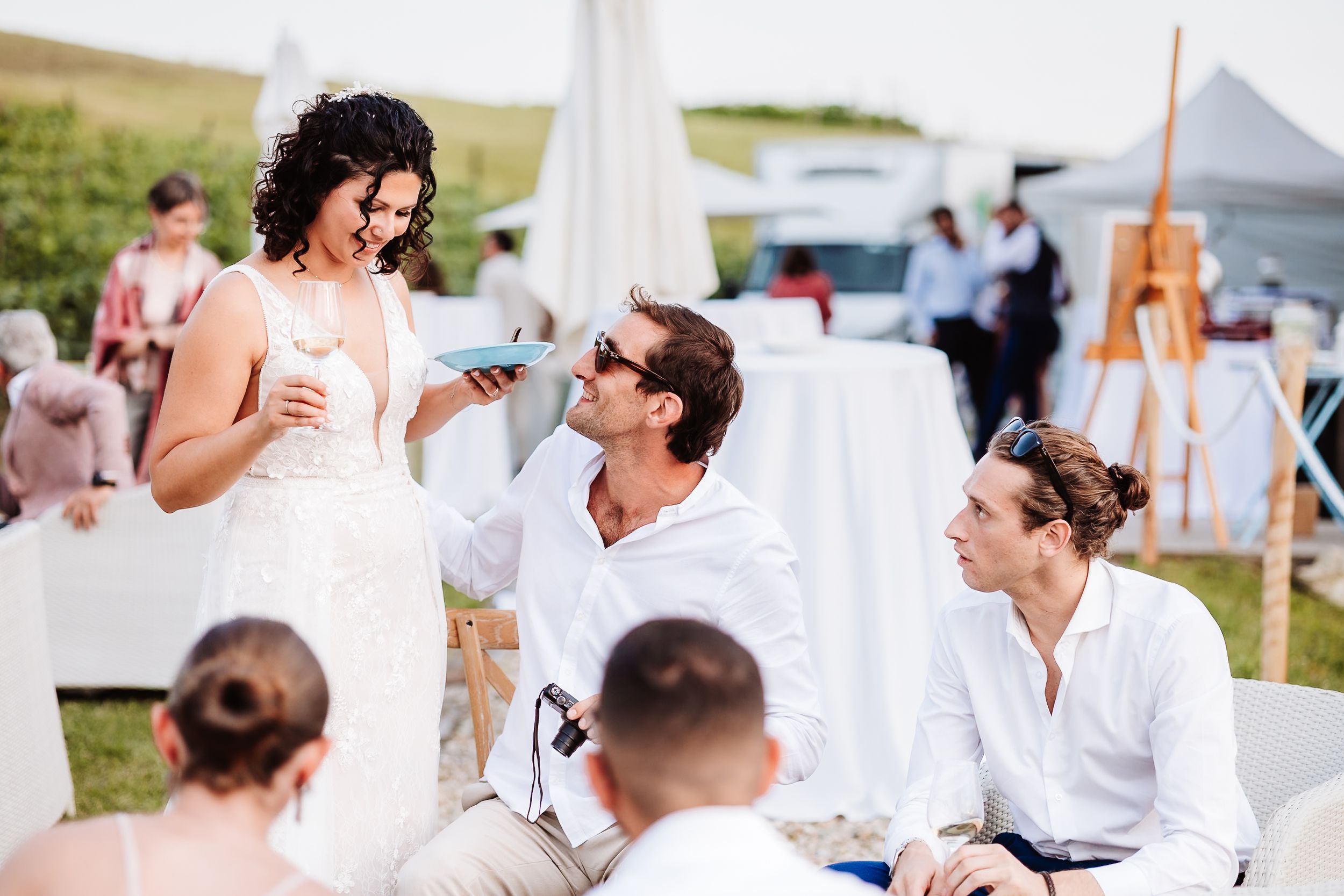 Guests in white attire socializing outdoors at an elegant garden wedding reception on a sunny day.