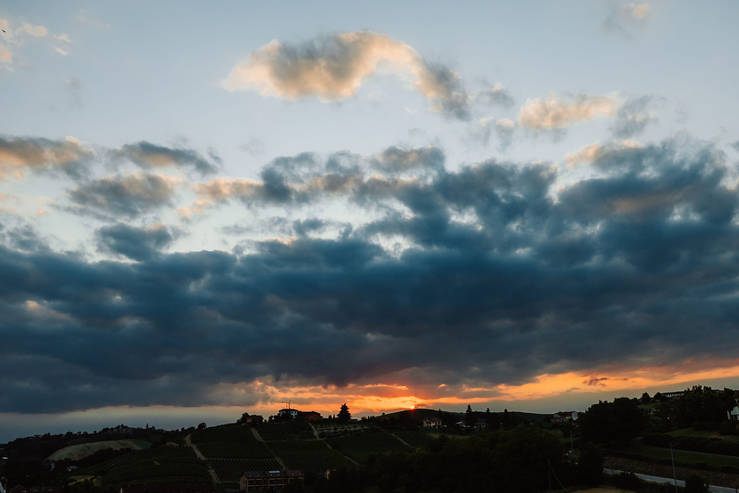 Dramatic sunset sky with dark storm clouds illuminated by orange and golden light over a silhouetted town.