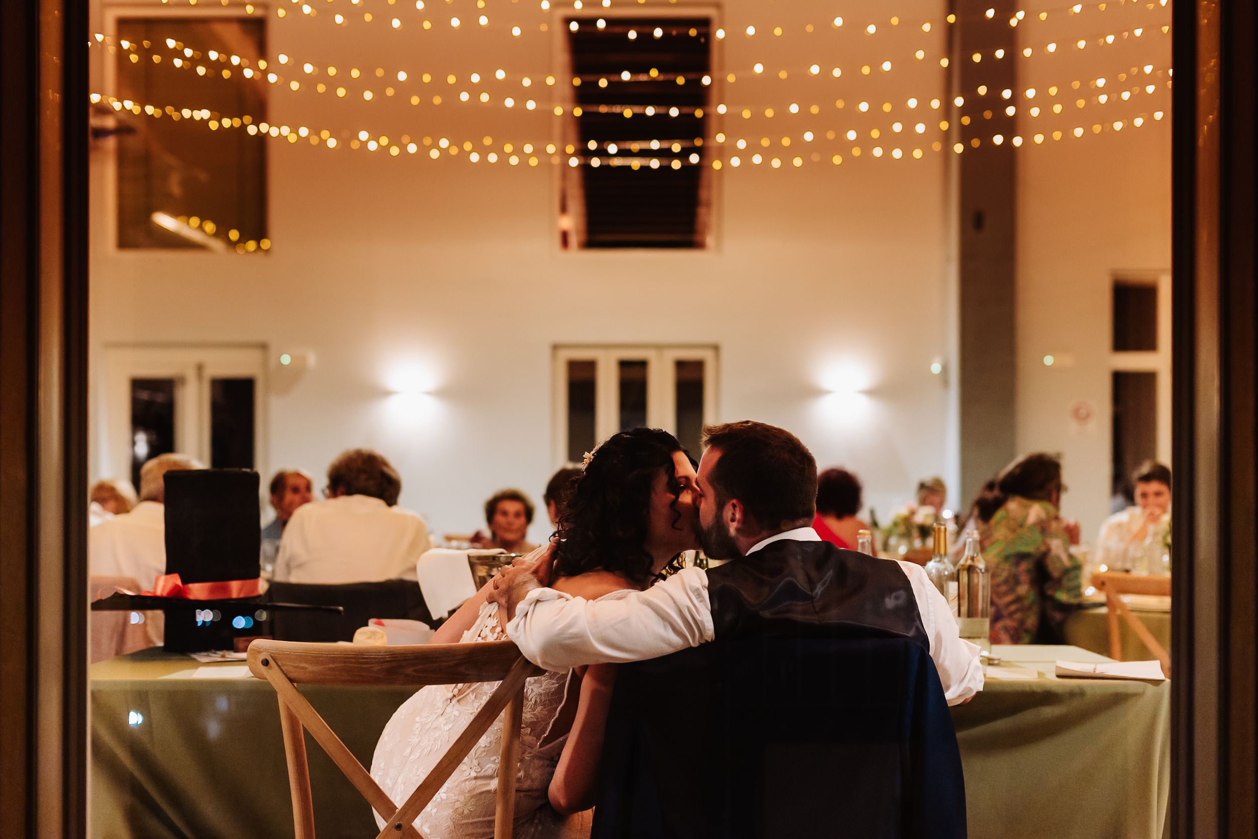 Bride and groom share a romantic moment at their wedding reception under warm string lights.