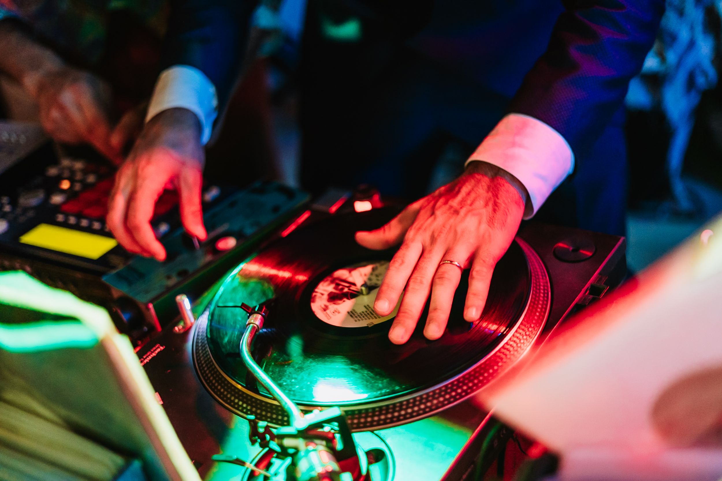 DJ spinning vinyl records on turntables under colorful neon lights at a live music event.