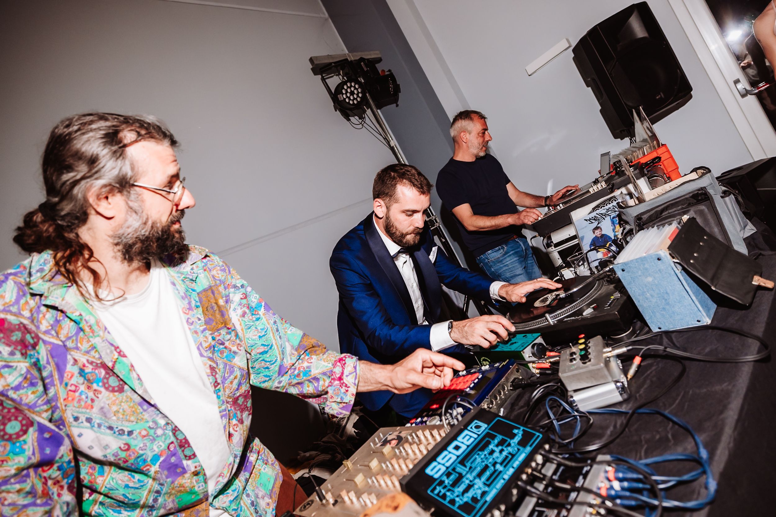 Three men operating DJ equipment and mixing console at a wedding reception event.