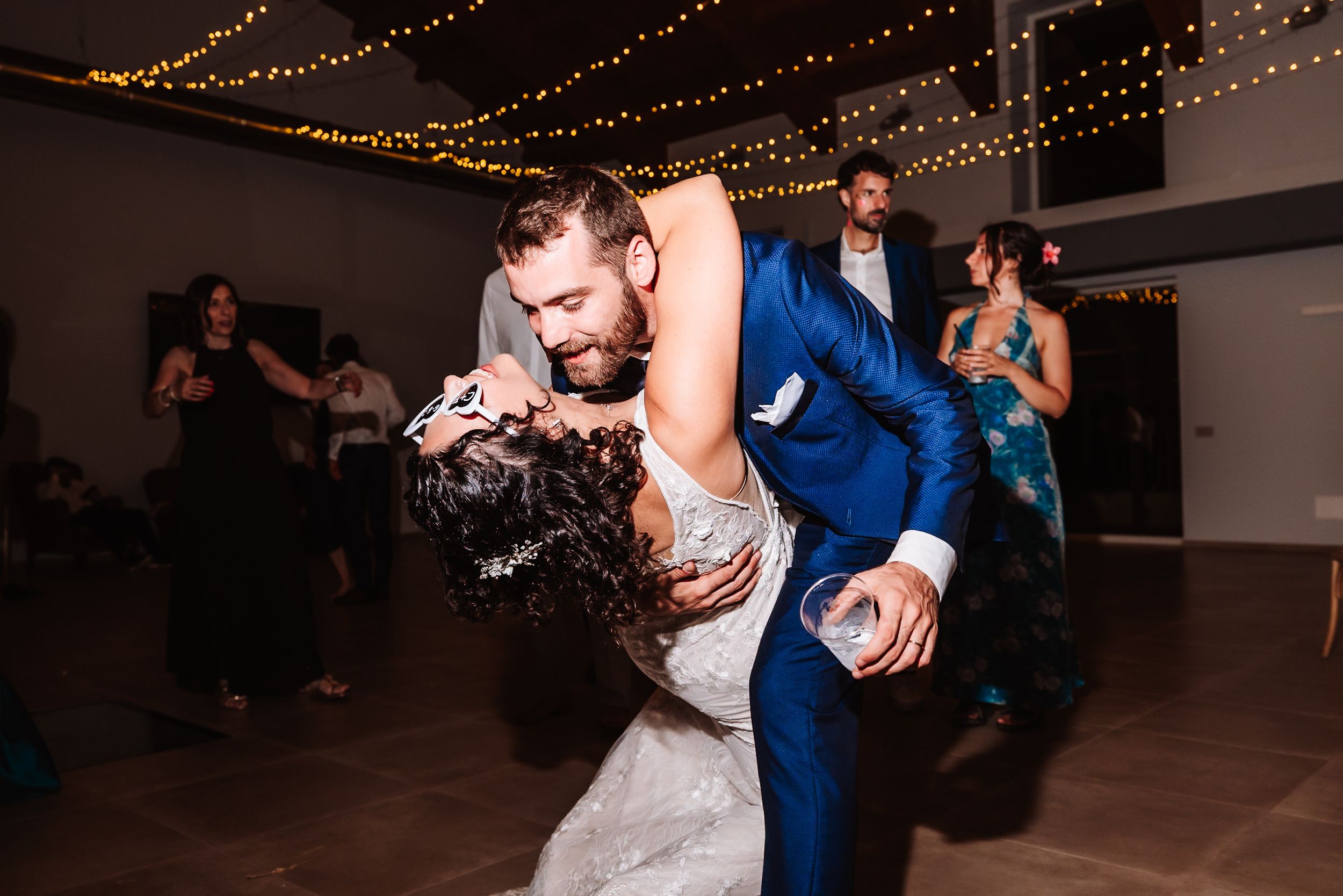 Bride and groom share a romantic dip dance at their wedding reception with guests celebrating in the background.