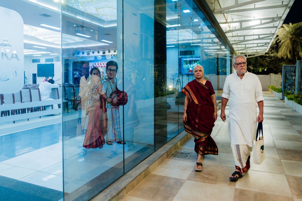 Elderly Indian couple in traditional attire walking outside a modern glass building at dusk.