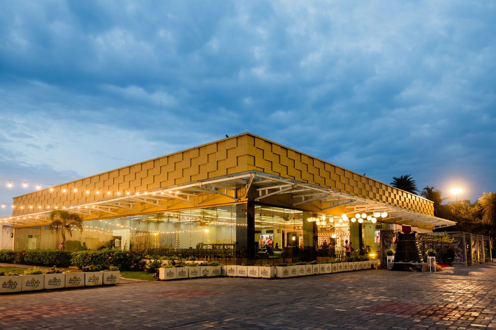 Elegant banquet hall exterior illuminated at dusk with warm lights under dramatic cloudy sky.