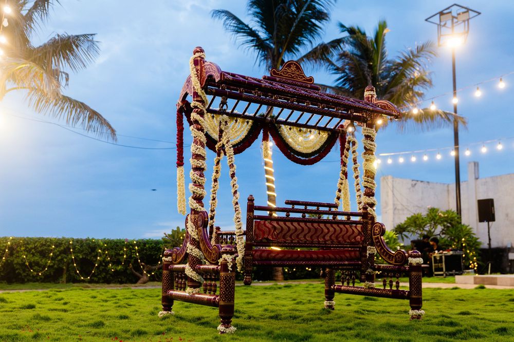 Traditional Indian wedding mandap swing adorned with flowers and string lights at dusk.