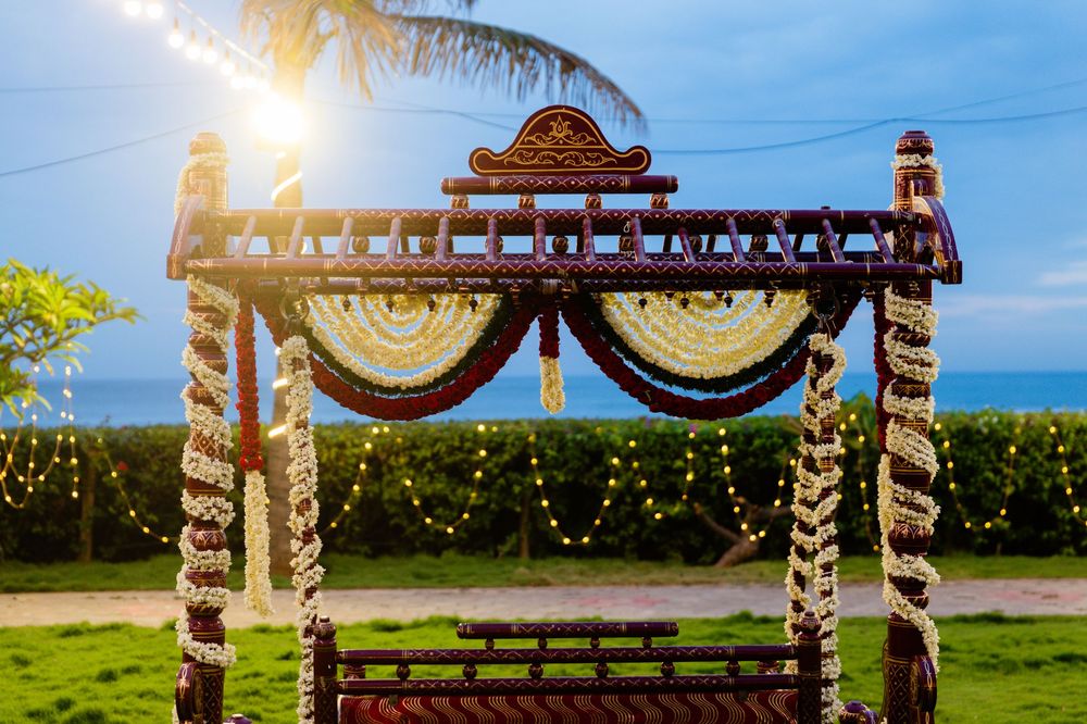 Beautifully carved wooden wedding mandap decorated with white flower garlands and fairy lights at beachside venue.