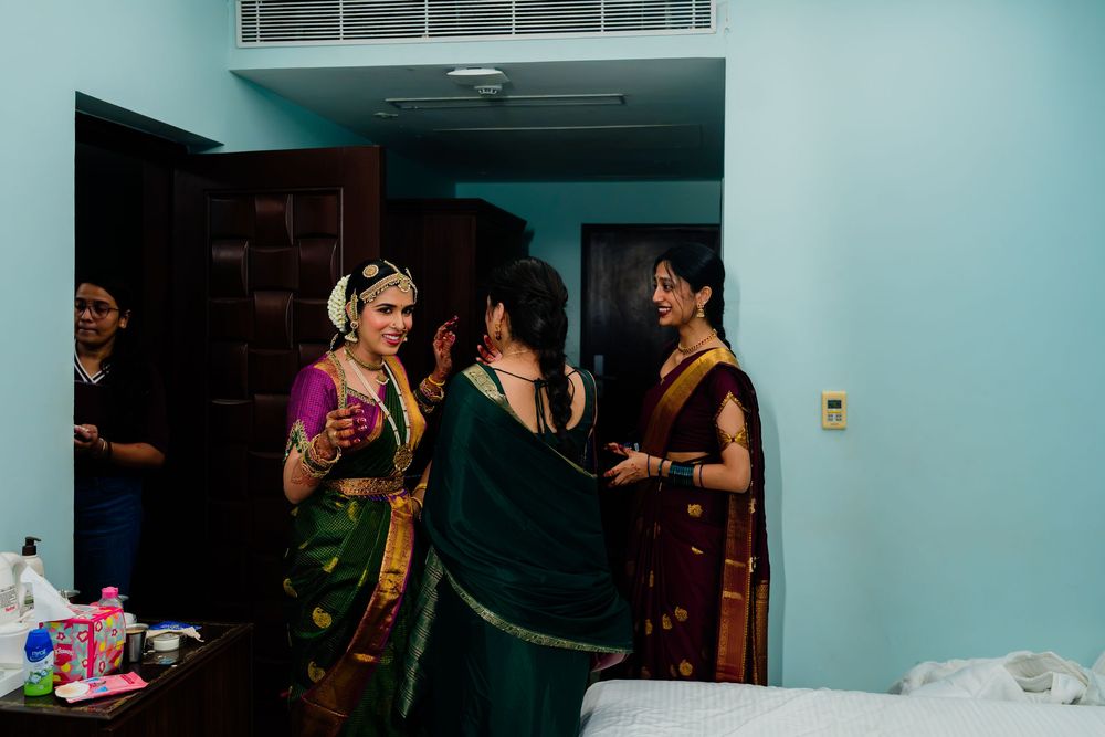 Indian bride in purple saree getting makeup done by family members in hotel room before wedding ceremony.