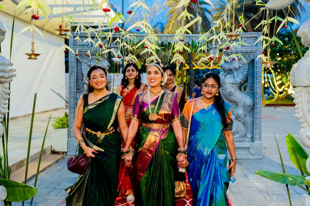Four women in vibrant traditional Indian sarees pose together outdoors at a festive cultural celebration.