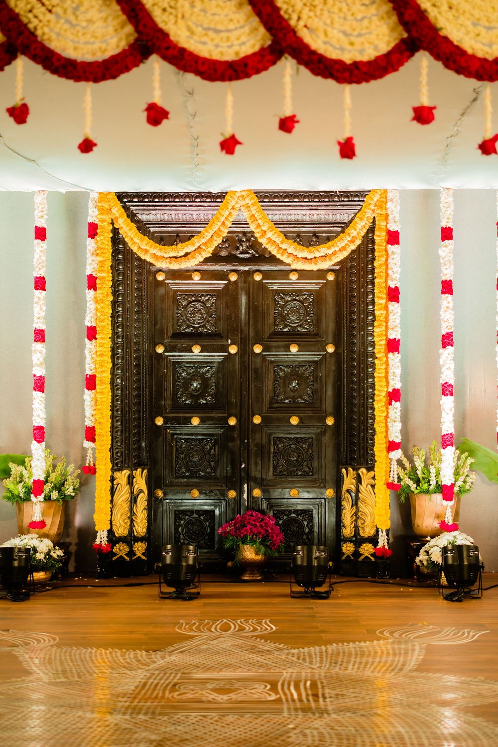 Ornate dark wooden temple doors adorned with yellow and red flower garlands for a traditional South Indian wedding ceremony.