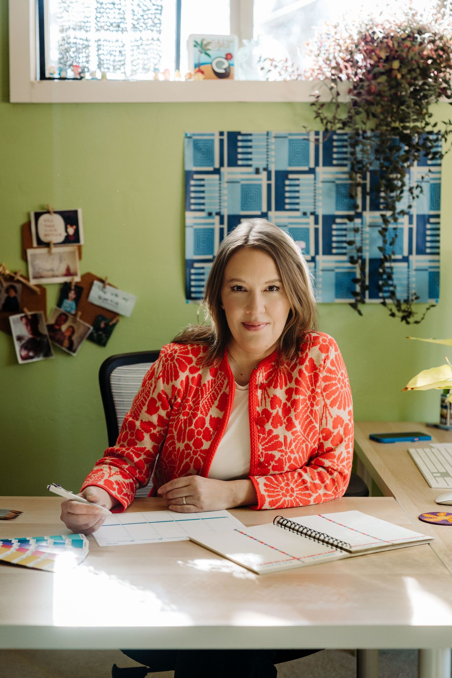 Smiling woman in bright orange blouse standing in a warmly decorated room with artwork on the walls.