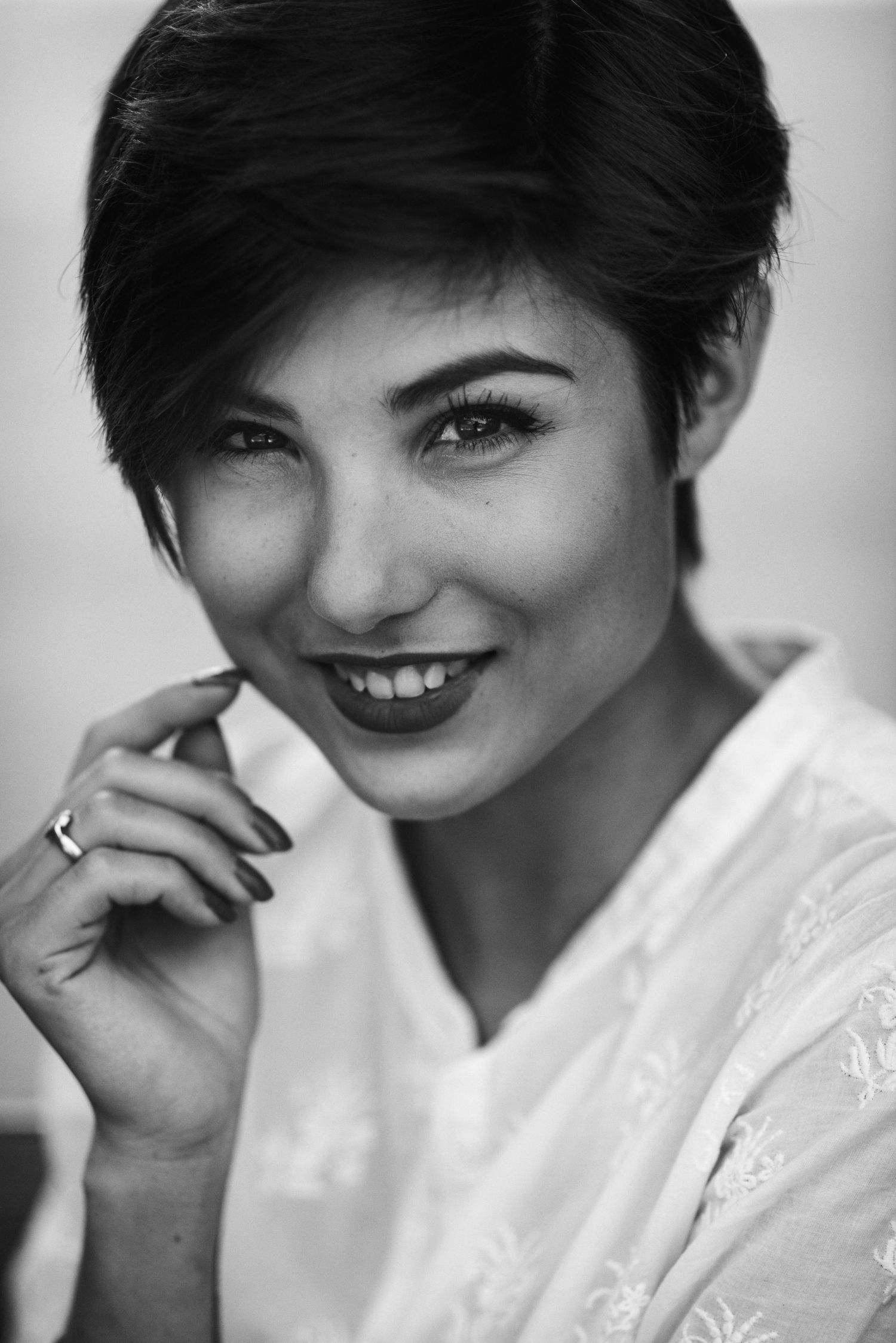 Primo piano in bianco e nero di una Giorgia Soleri sorridente con capelli corti scuri, che sfiora delicatamente il viso con una mano