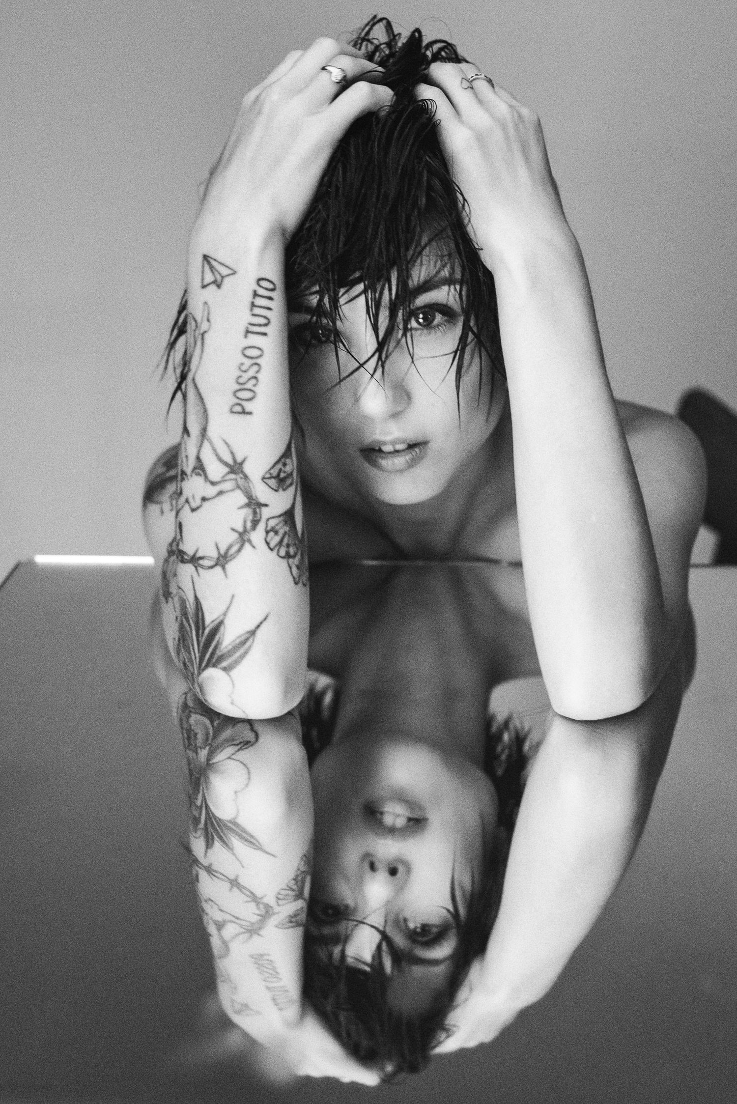 Scatto artistico in bianco e nero di Giorgia Soleri con le mani tra i capelli bagnati e braccia tatuate, fotografata mentre si specchia