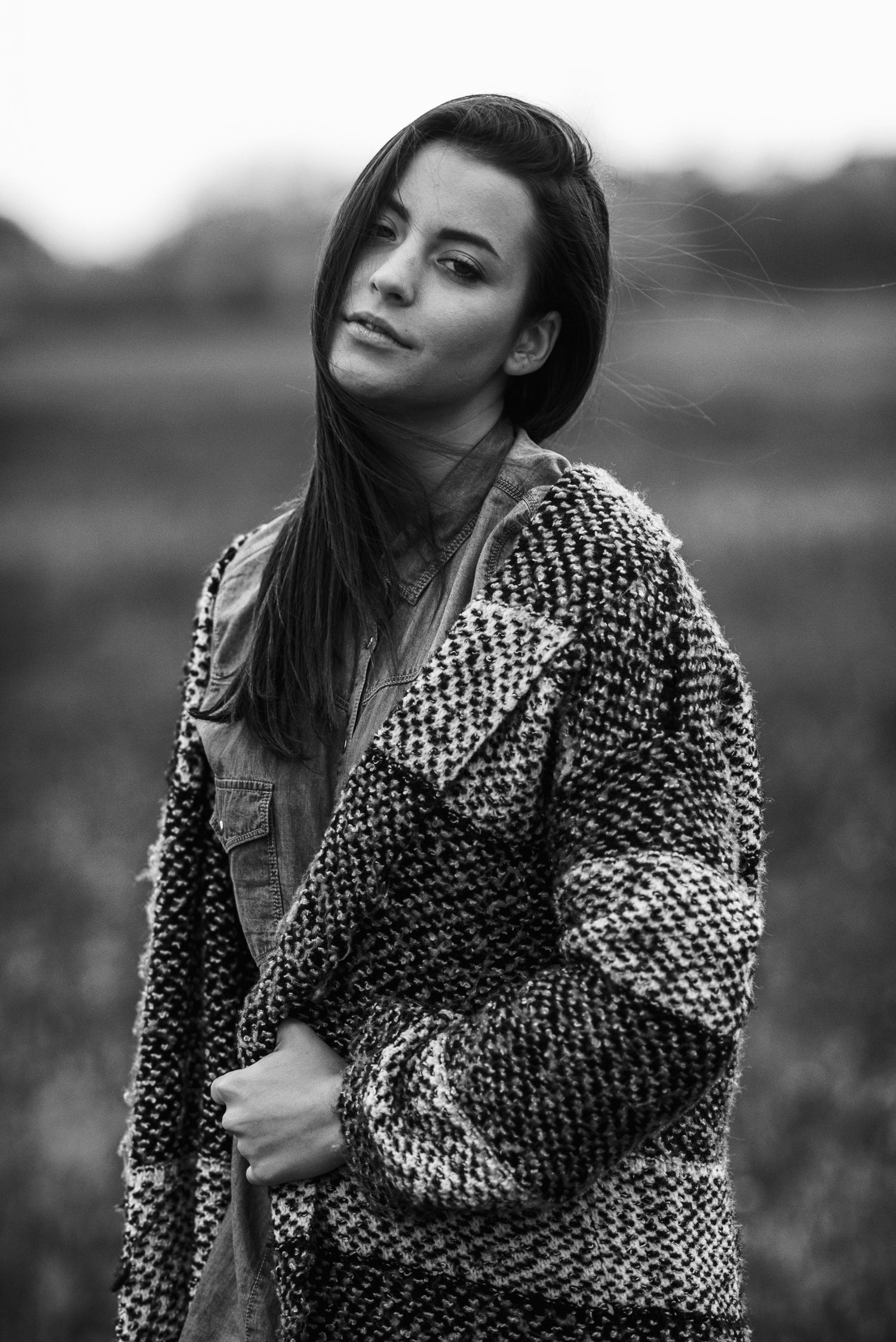 Primo piano in bianco e nero di una ragazza con cappello stile marinaio e cappotto scuro, appoggiata a una parete mentre guarda di lato.