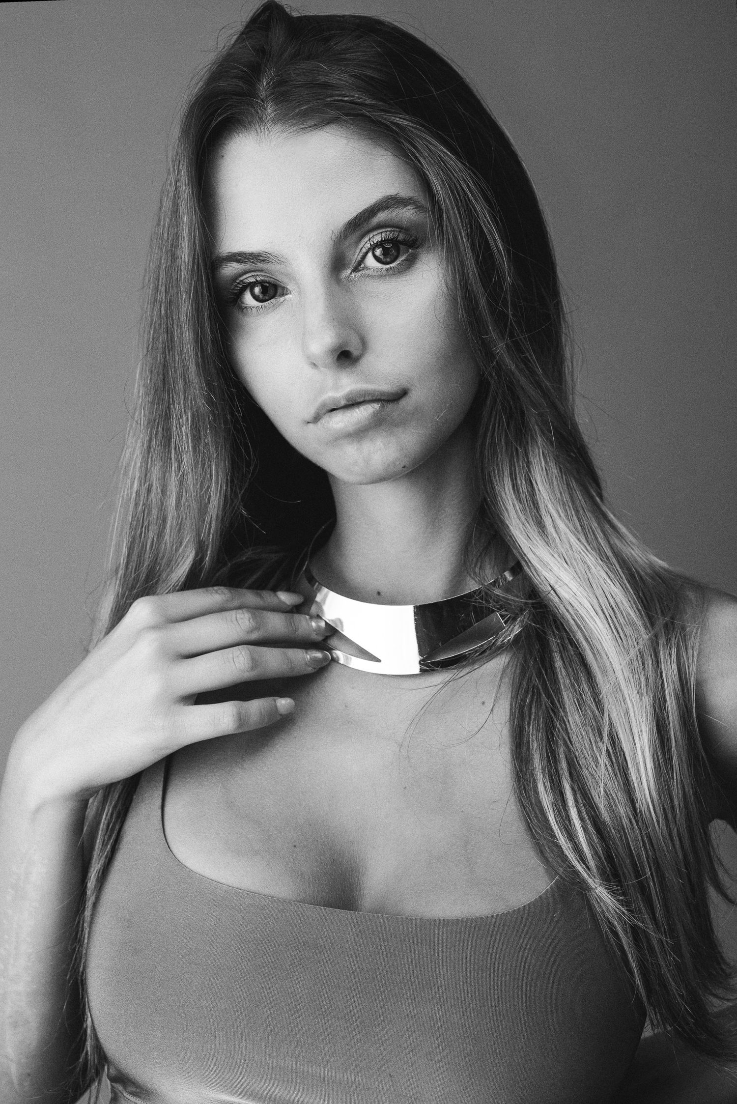 Ritratto di bellezza in bianco e nero di una ragazza con lunghi capelli lisci che sfiora una collana rigida in metallo argentato sul collo.