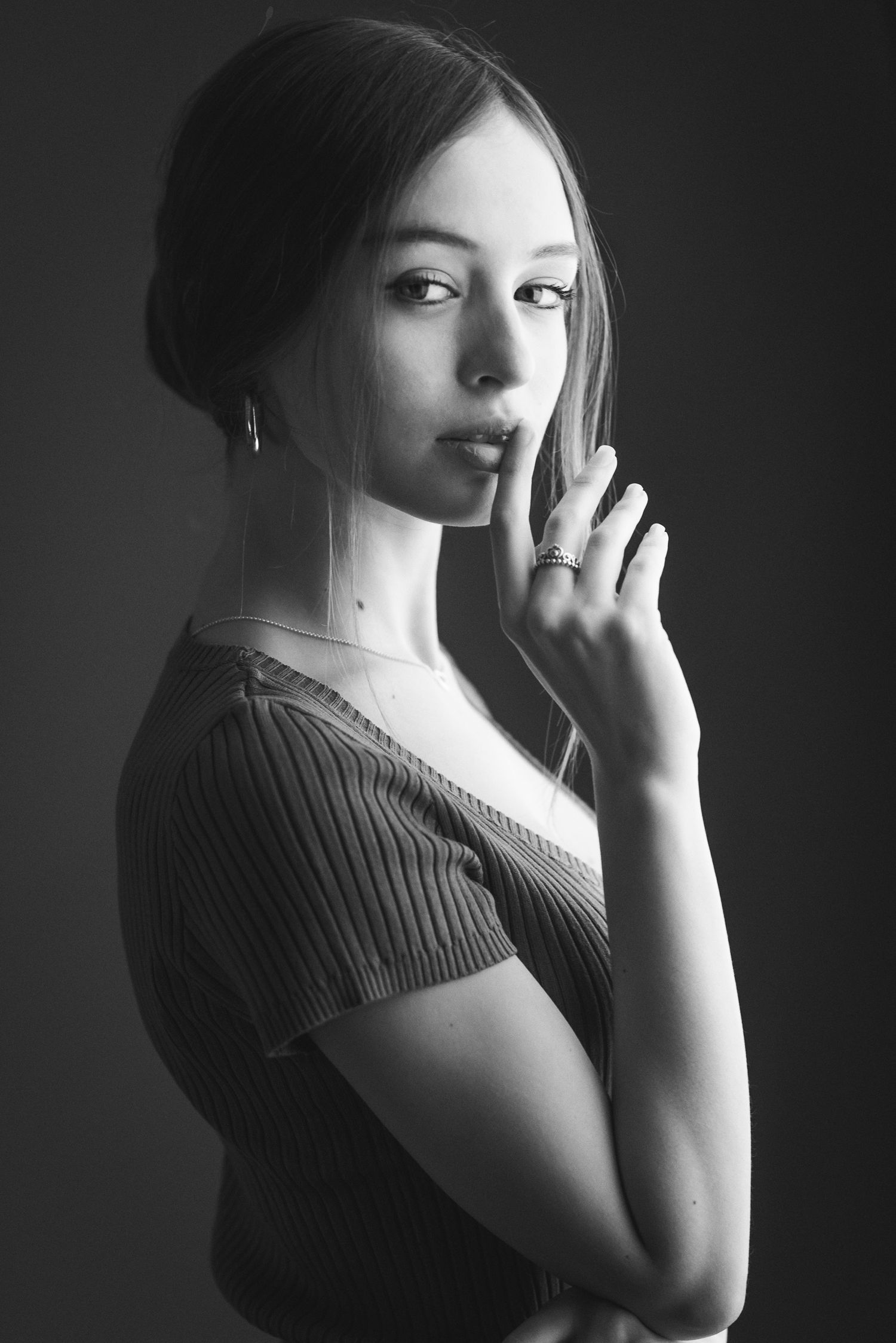 Ritratto di profilo in bianco e nero di una giovane donna che sfiora delicatamente le labbra con un dito guarda la fotocamera.
