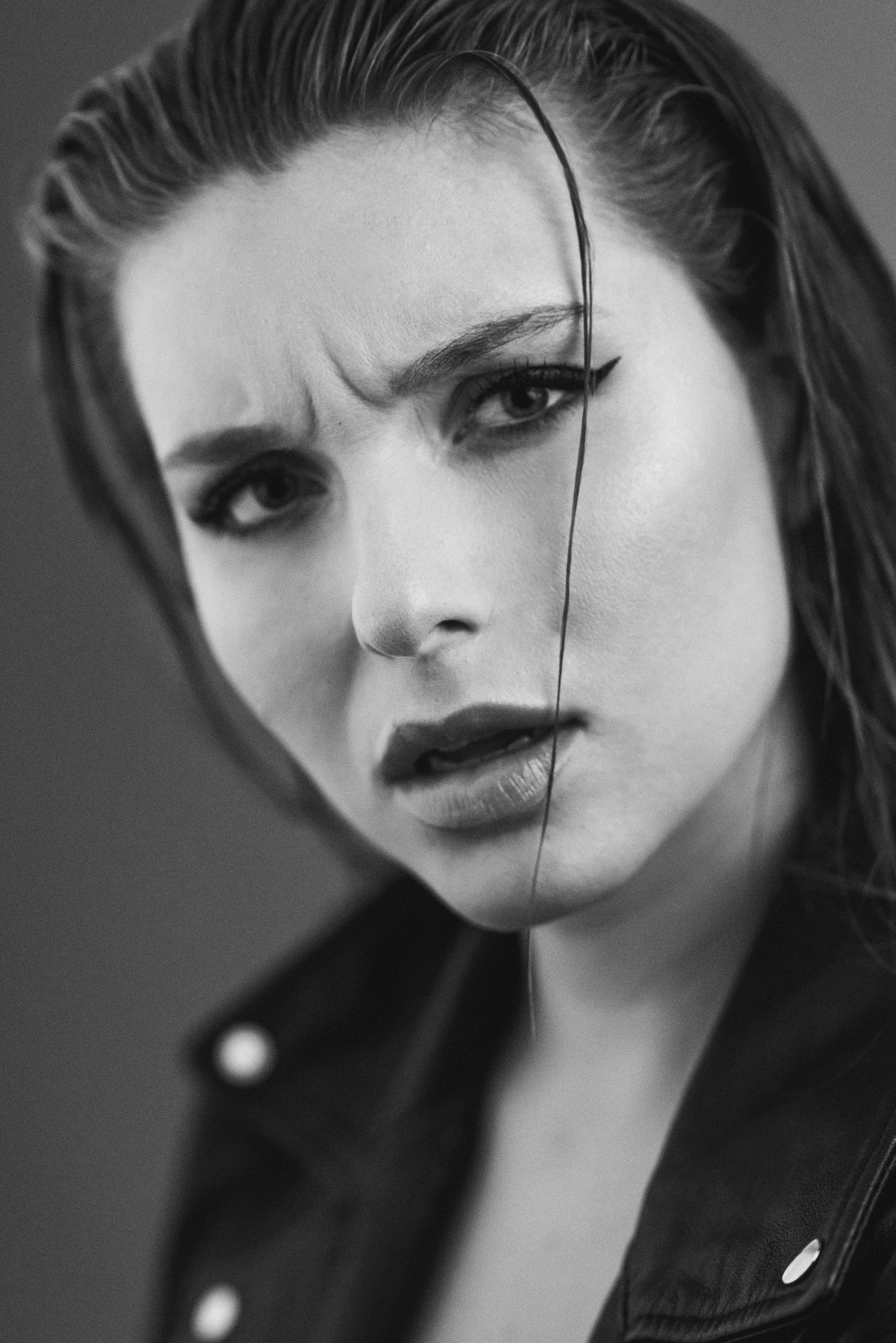Primo piano ravvicinato in bianco e nero di una donna con giacca di pelle ed eyeliner marcato, con un'espressione del viso decisa e dubbiosa