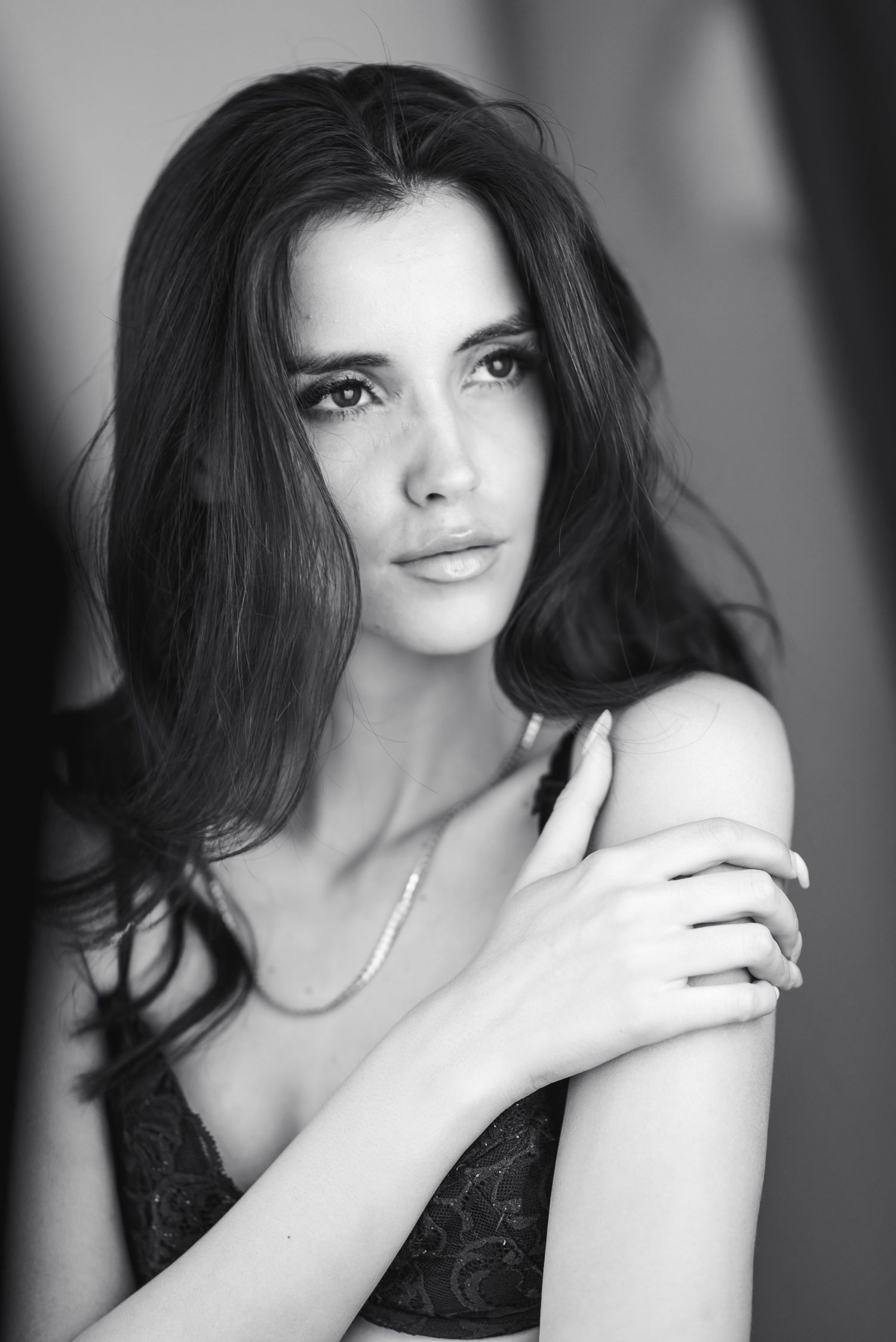 Ritratto fotografico in bianco e nero di una donna con lunghi capelli scuri sciolti e una mano posata sulla spalla, mentre guarda leggerment