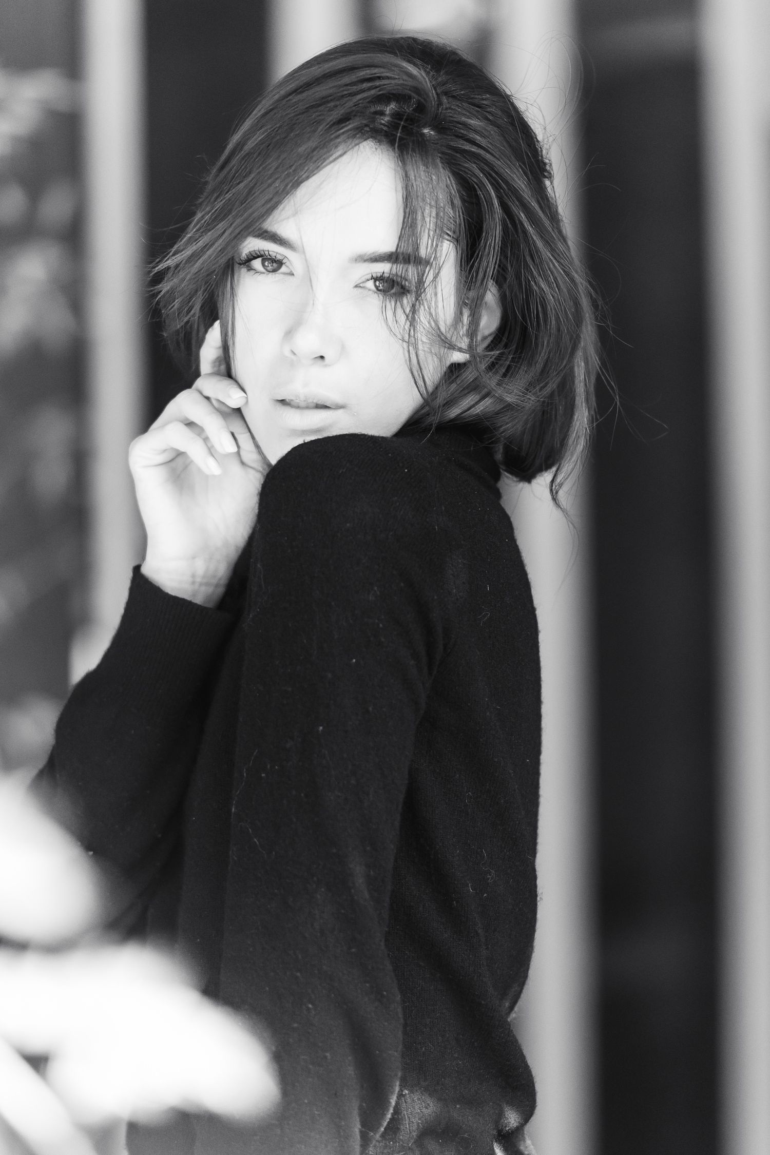 Ritratto in bianco e nero di una donna che indossa un maglione nero a collo alto, posando con la mano vicino al viso e lo sguardo rivolto ve