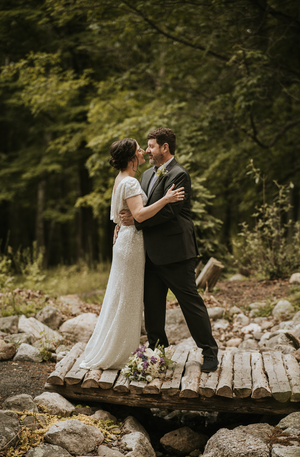 a couple kissing on their wedding day, standing on top of a small bridge in the woods