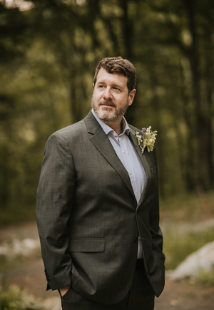 a husband posing for his wedding day portrait session, green foliage and dark suited