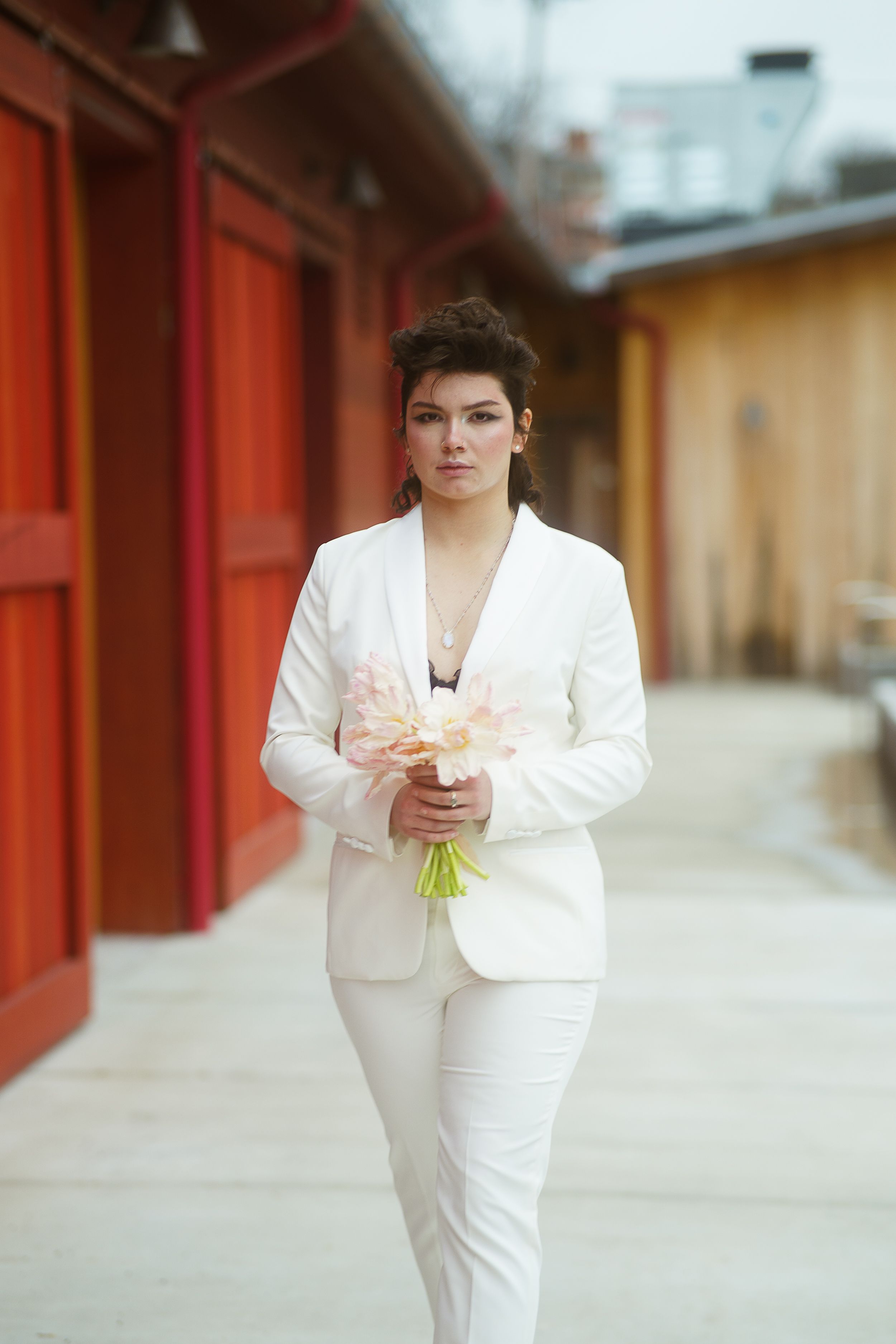 a young woman walking towards the camera with flowers in her hand and in a white suit on her wedding day