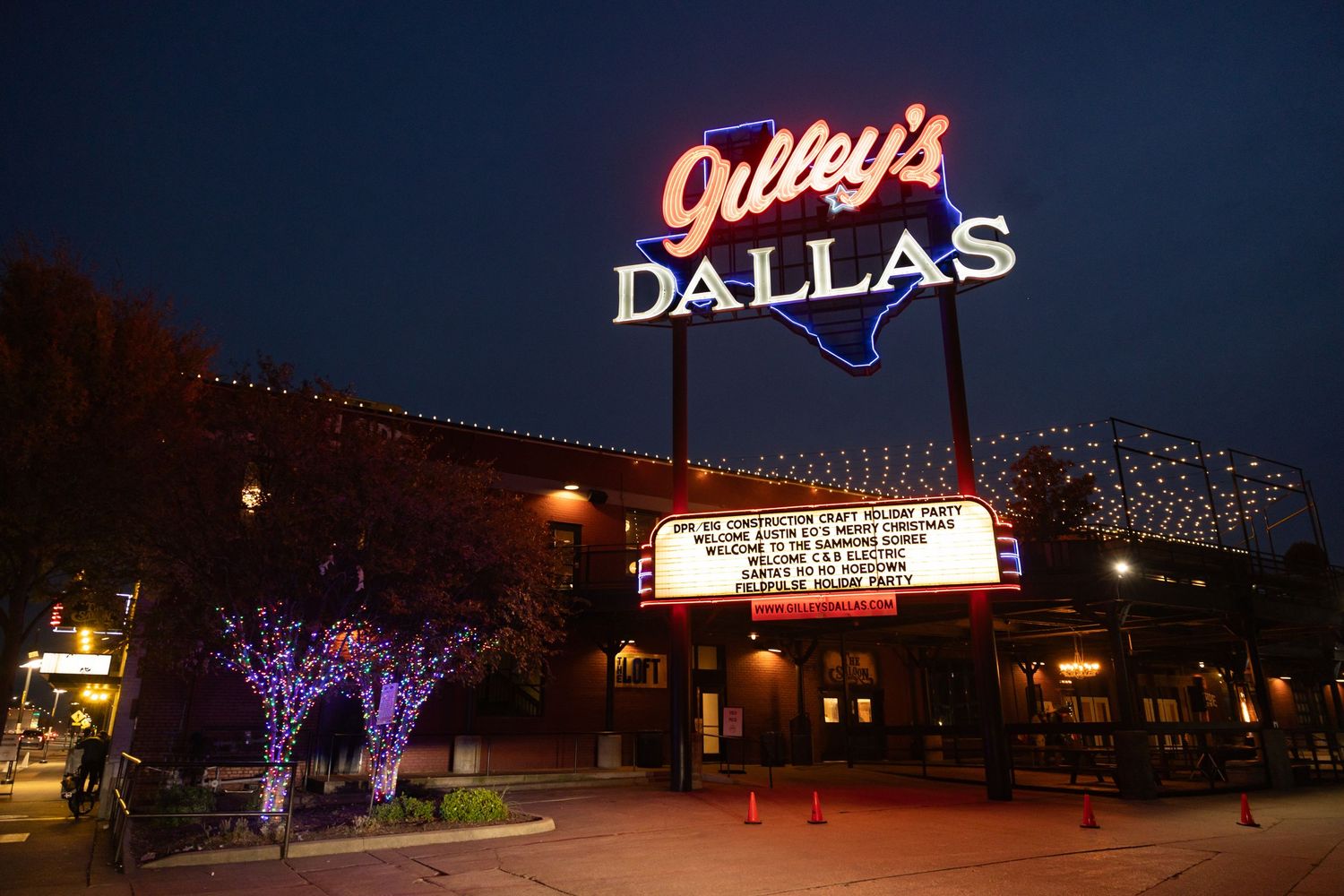 Gilley's Dallas neon sign illuminated at night with marquee lights and festive tree decorations outside the venue.