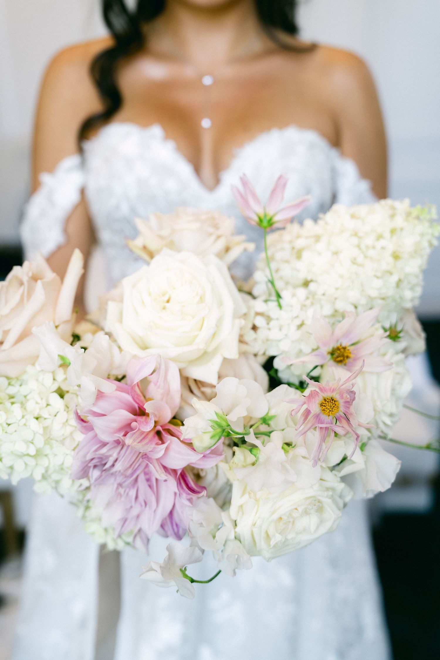 Bride in strapless white gown holding lush bridal bouquet of white roses, pink cosmos, and hydrangeas.