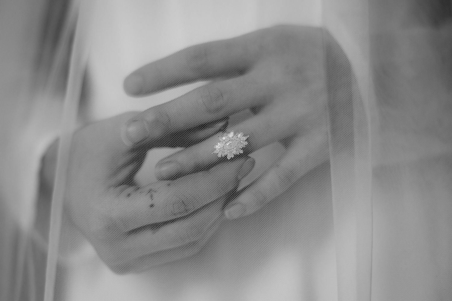 Close-up black and white photo of bride's hands wearing a stunning floral diamond engagement ring on wedding day.