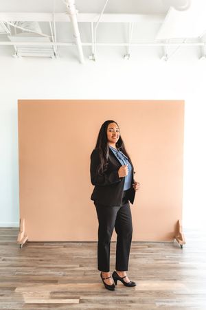 Professional woman in black blazer and blue blouse posing in modern studio space.
