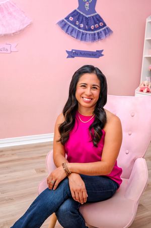 Woman in pink sleeveless top sits smiling in pink chair in ballet-themed pink room.