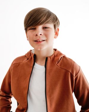Happy young boy in rust orange zip-up hoodie posing on white background.