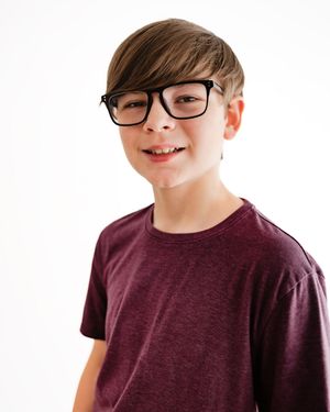 Smiling preteen boy with black glasses in maroon t-shirt on white background.