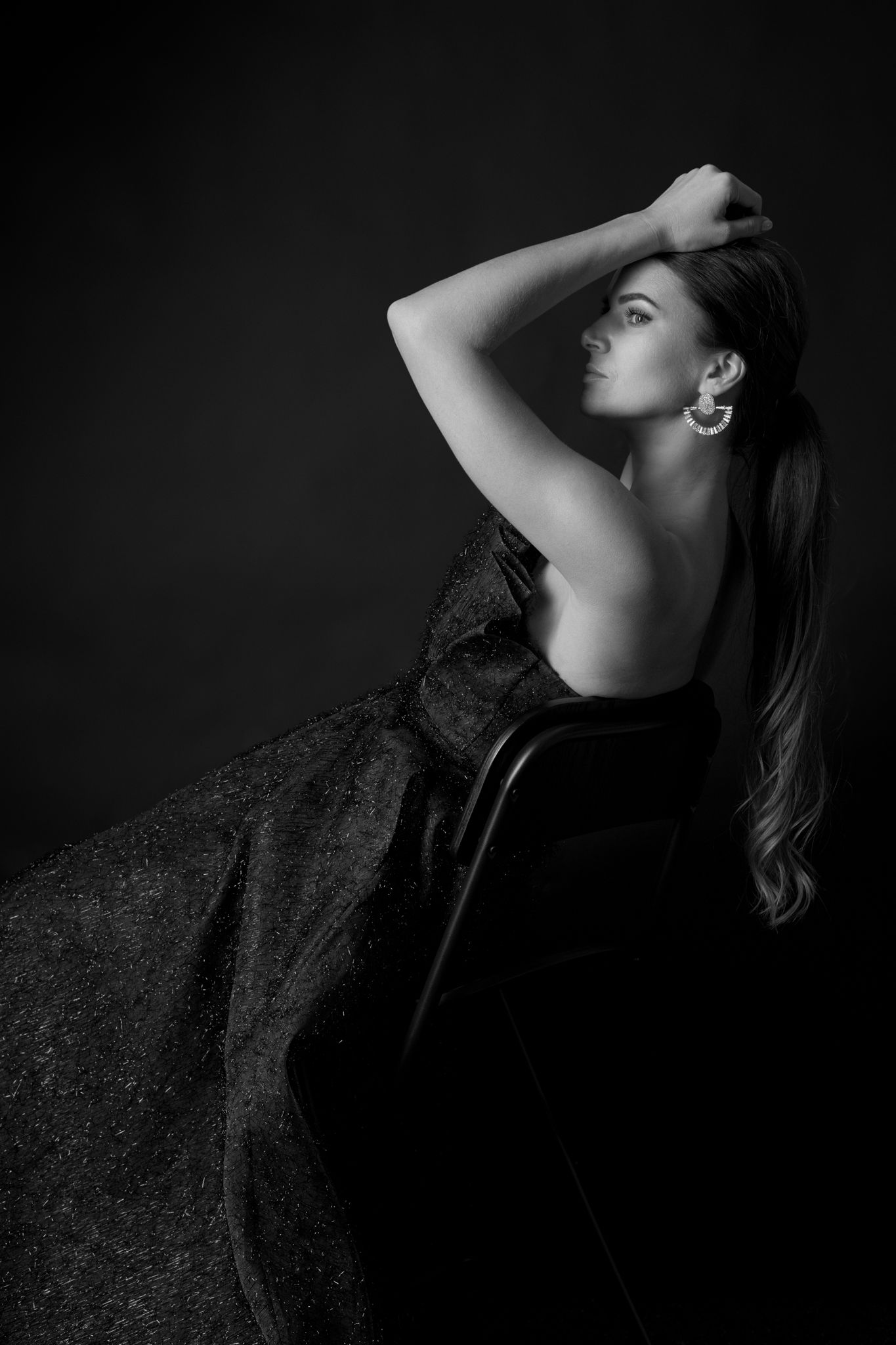 Black and white portrait of a woman in a strapless ball gown, arms crossed, against a dark background.