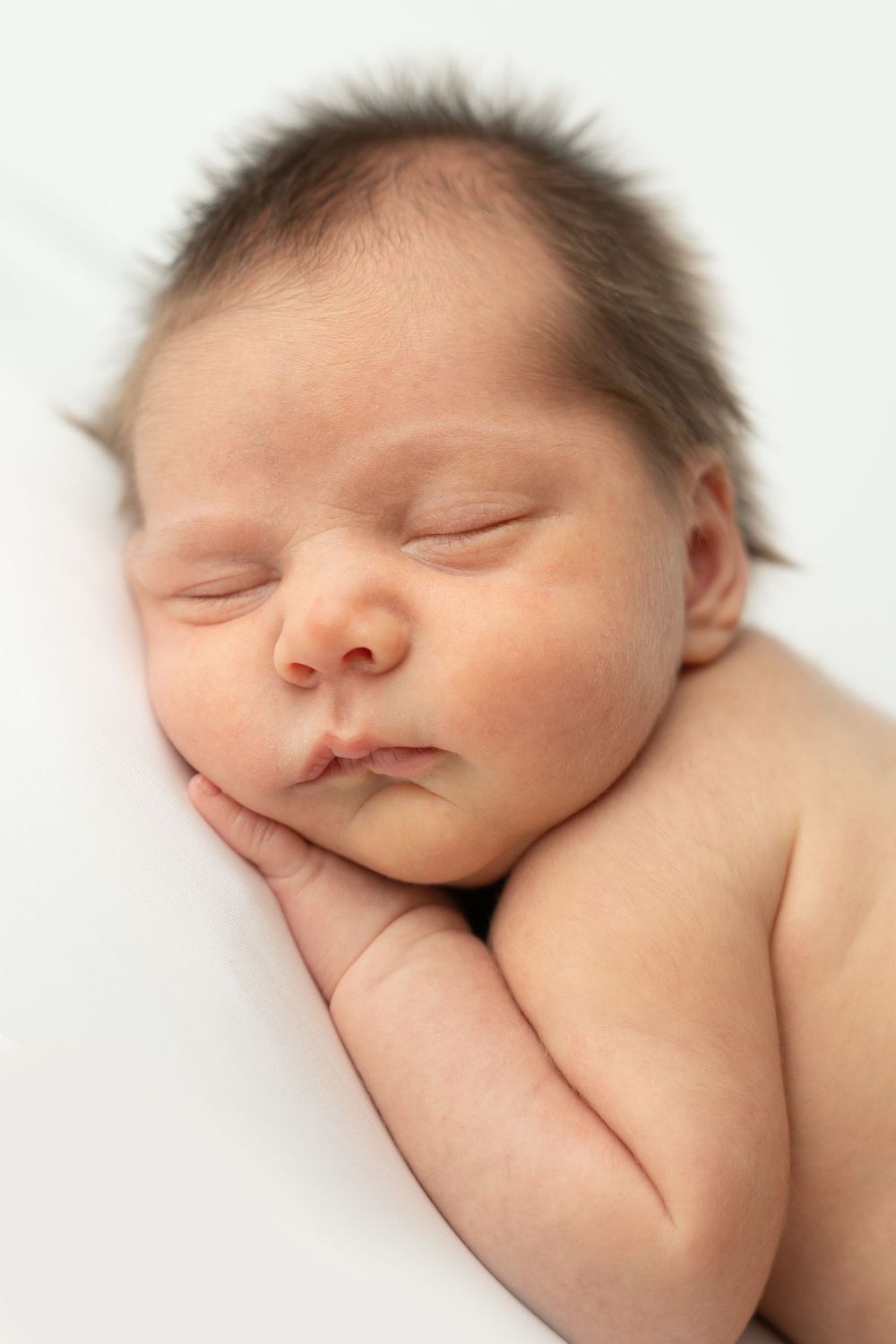 A peaceful newborn baby sleeping with hands tucked under cheek on a white background.