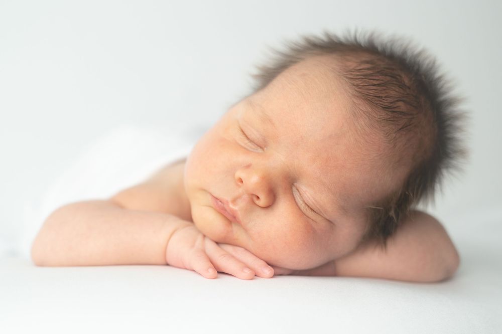 Peaceful newborn baby sleeping with hands under chin on white background, perfect newborn photography portrait.
