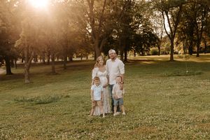 Family of five posing in a sunlit park during golden hour, with parents and three young children on green grass.