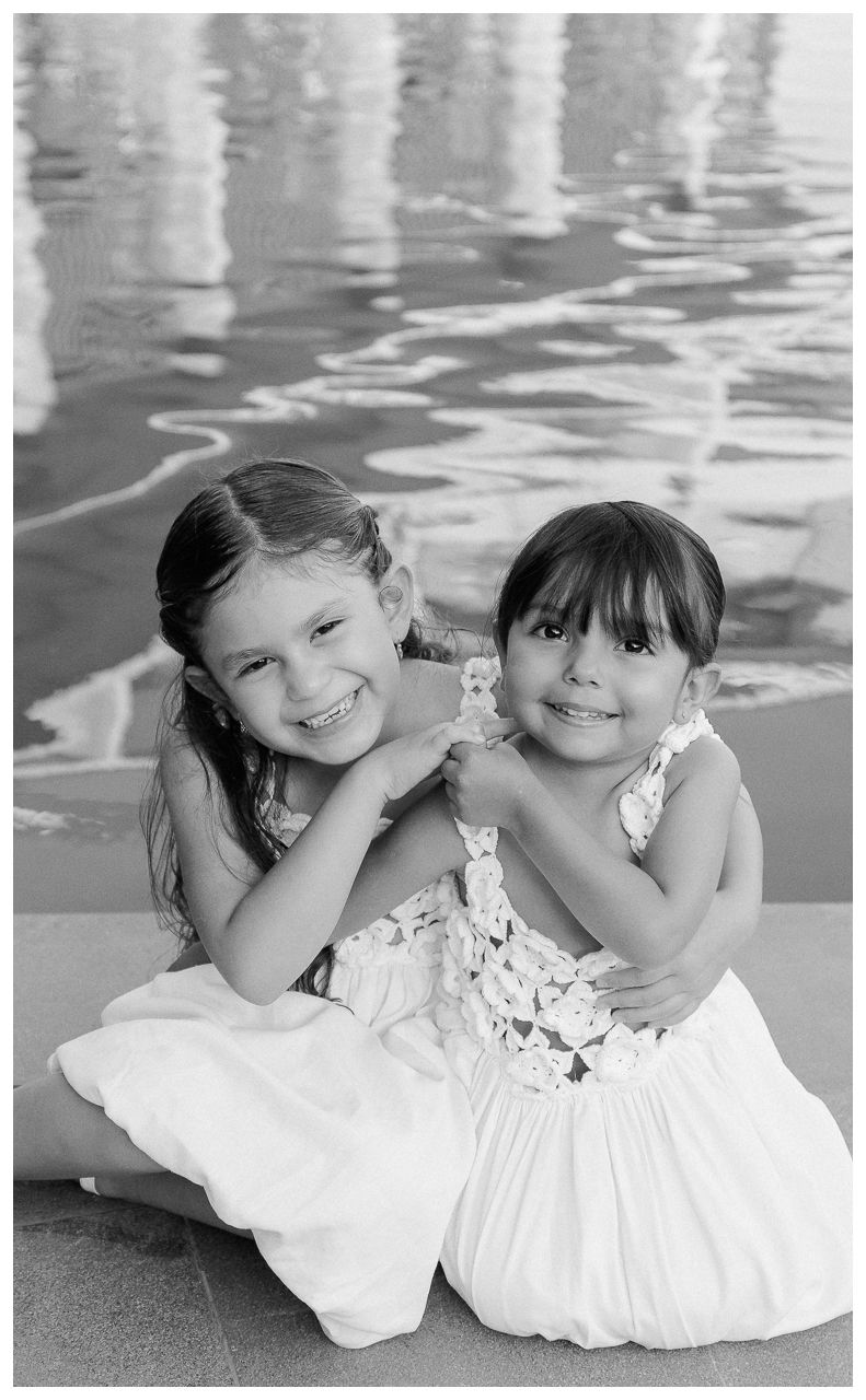 Dreams Bahia Mita family photographer capturing two sisters smiling together by the pool in white dresses.
