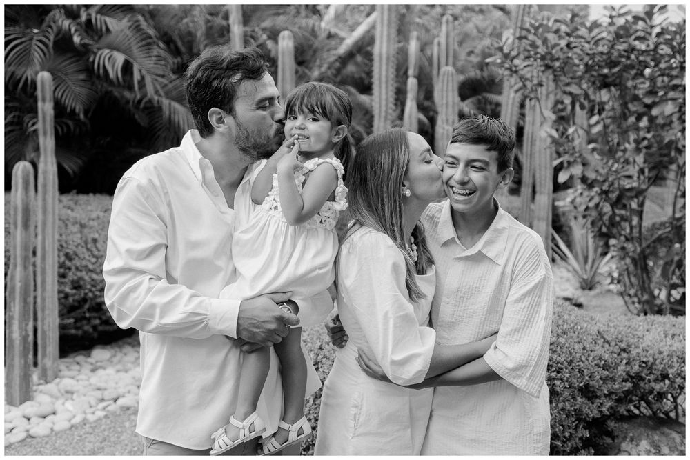 Family photo session at Dreams Bahia Mita with parents sharing a kiss as their children smile nearby, capturing a relaxed vacation moment.