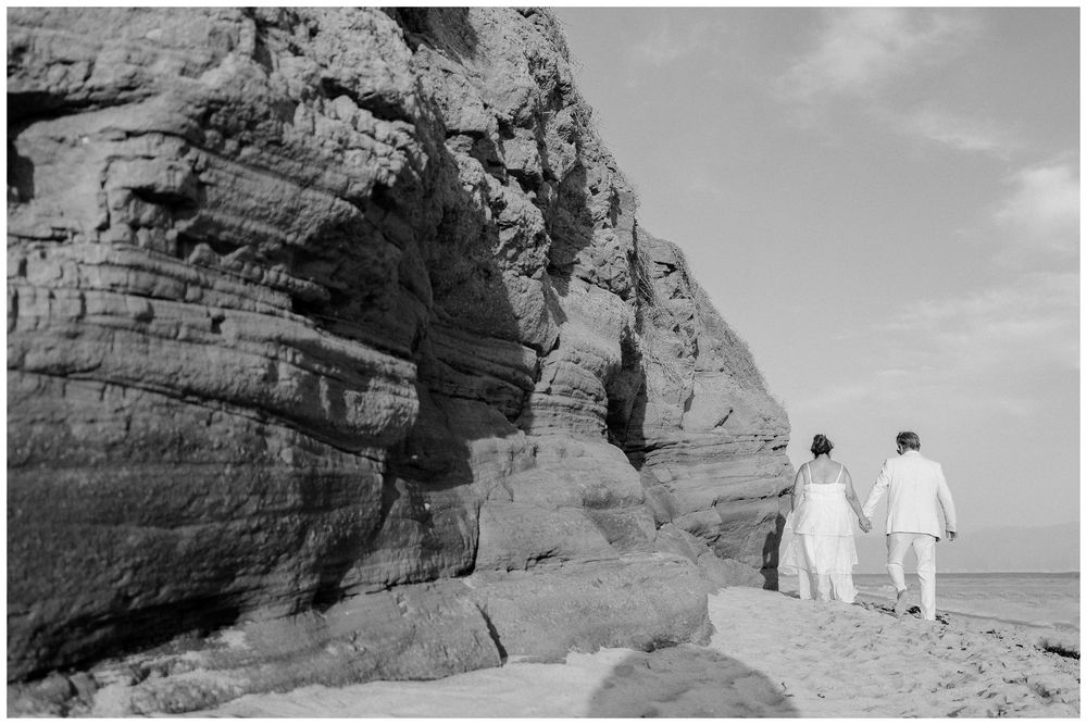 Couple enjoying a beach photo session at Dreams Bahia Mita, walking along the shore beside dramatic rock cliffs.